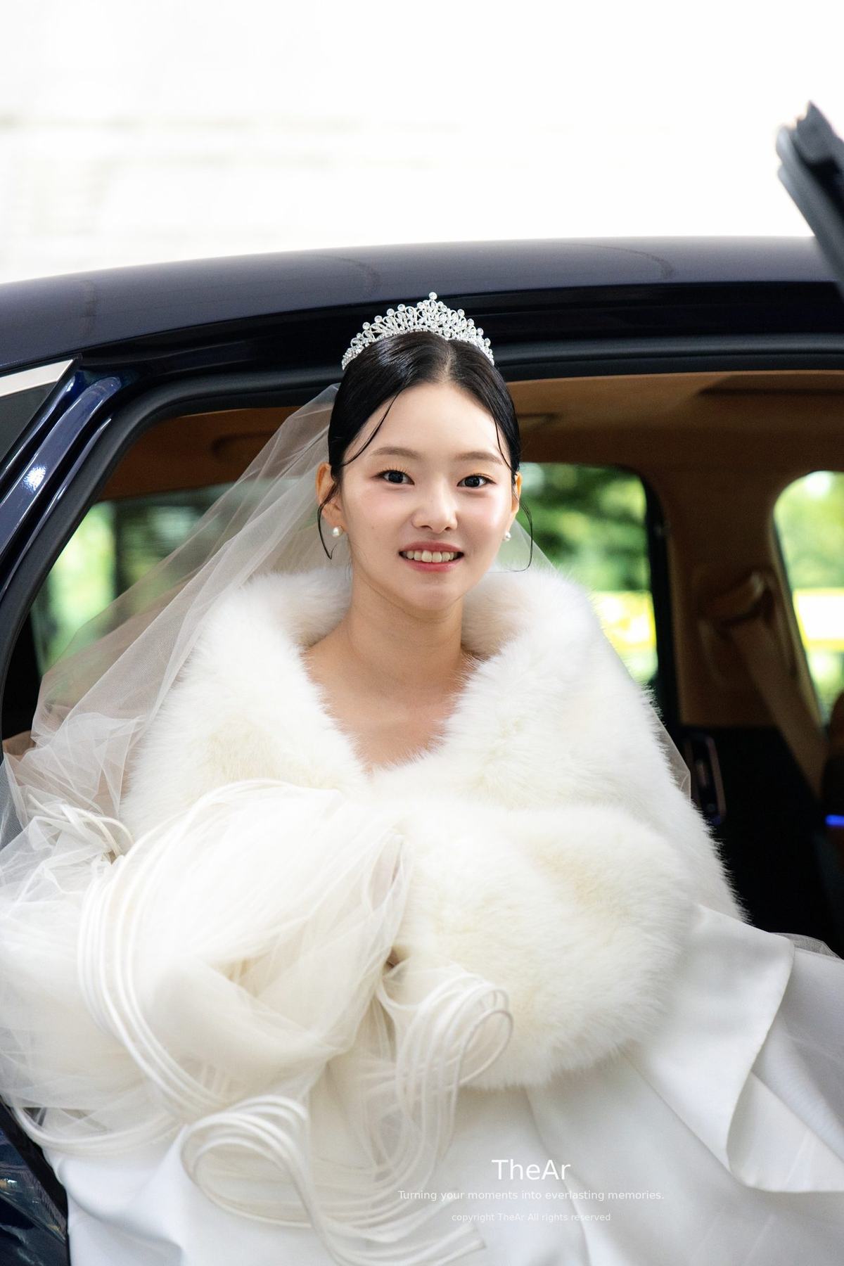 흰 퍼 케이프와 티아라 차림으로 웨딩카에서 내리며 웃는 분당 바실리움의 신부
