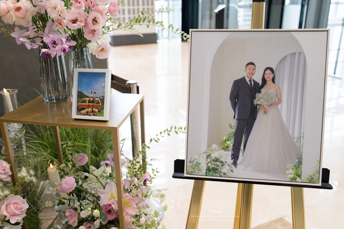 분당 바실리움 로비 웰컴 테이블에 놓인 웨딩 액자와 분홍 꽃 장식, 그 옆의 촛불