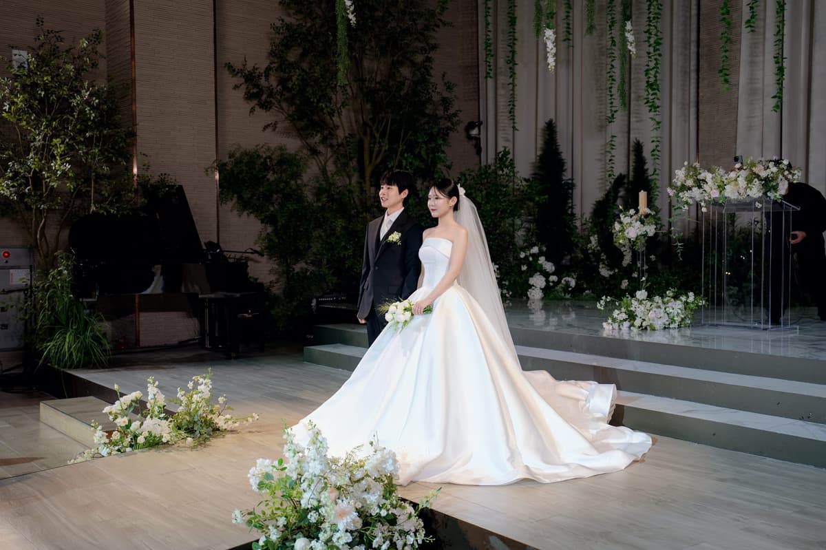 벽돌 기둥과 키 큰 나무가 선 베르테홀 단상, 계단 아래로 흐르는 드레스 자락