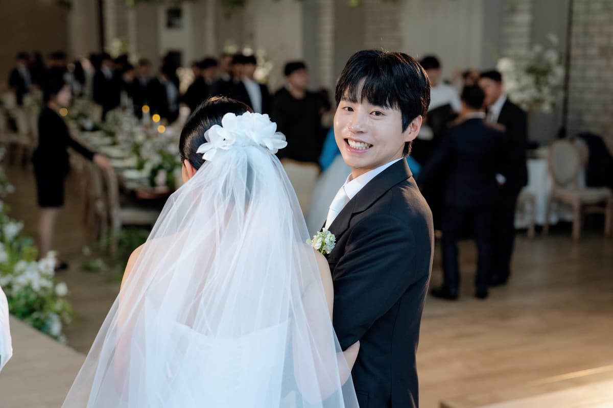 연회장에서 베일을 쓴 신부 곁에 서서 환하게 웃는 신랑