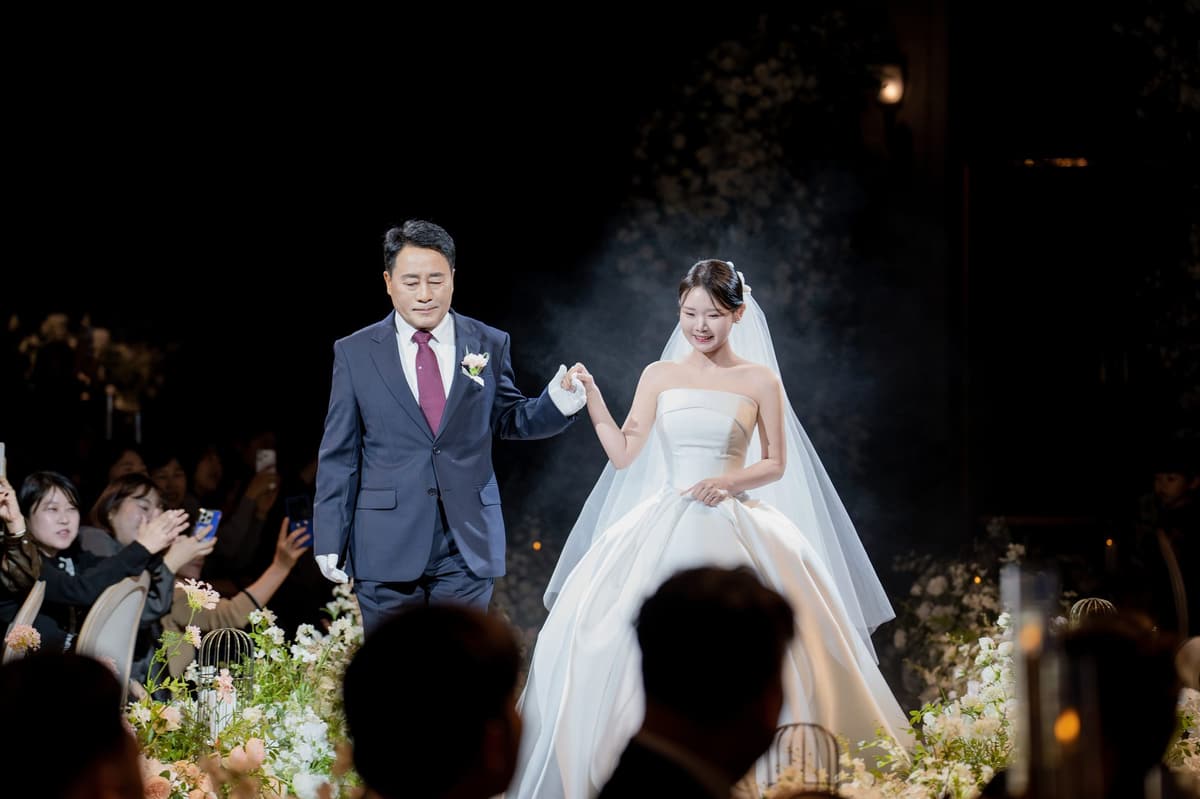 아버지가 신부의 손을 들어 올린 채 함께 버진로드를 걷는다
