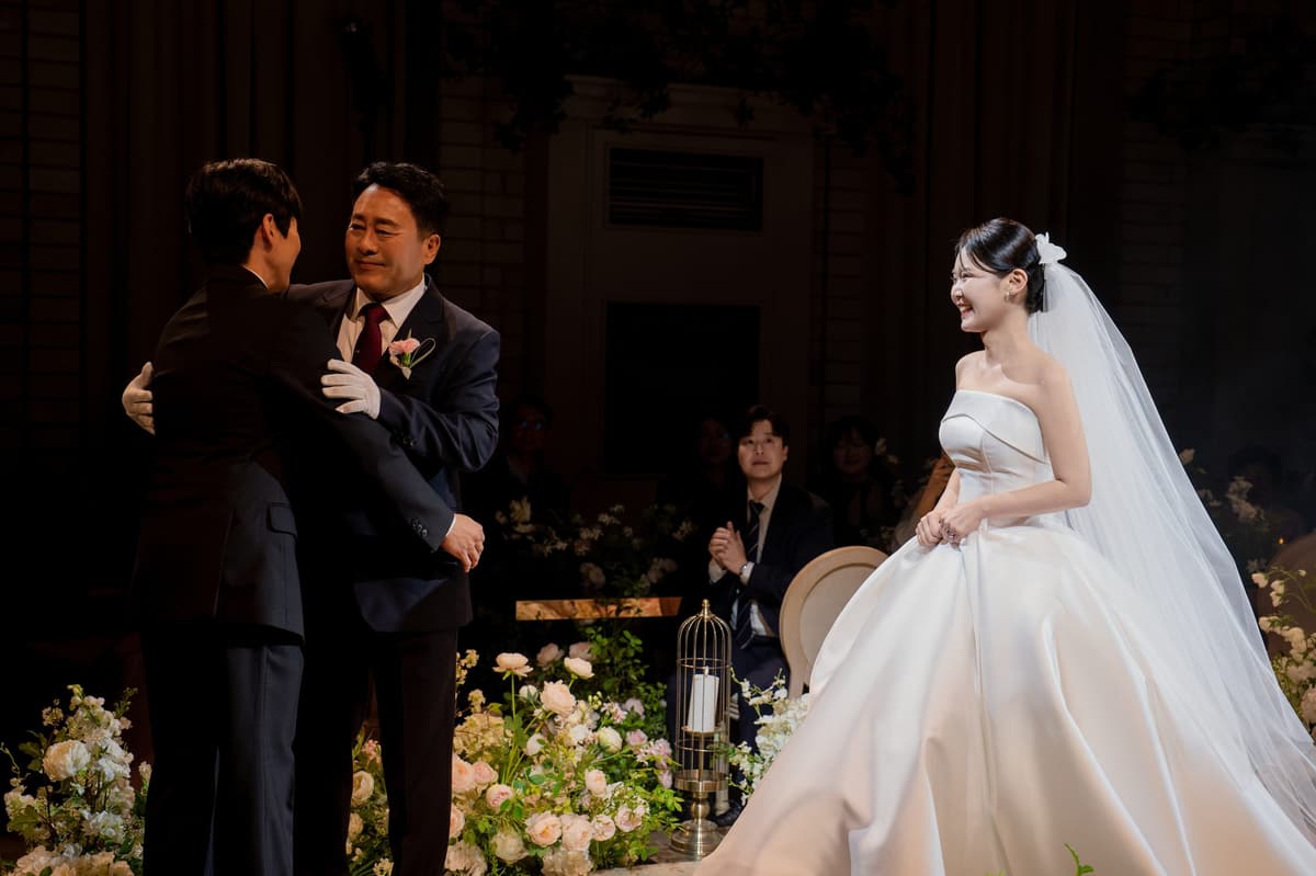신부를 건네준 아버지가 신랑을 끌어안고 그 옆에서 신부가 웃는다