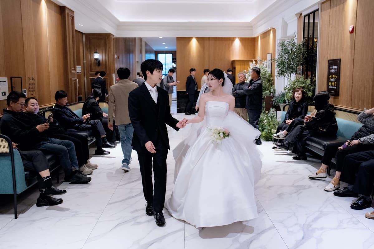 천안 비렌티 로비의 대리석 바닥을 하객들 사이로 손을 잡고 걸어가는 신랑과 신부
