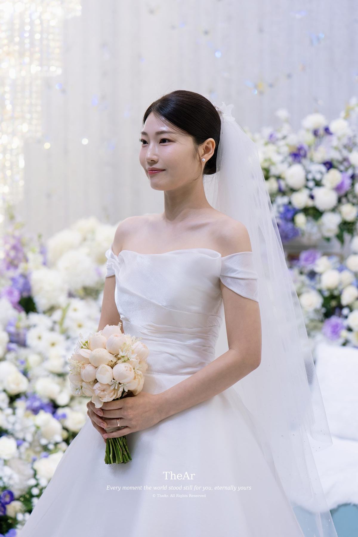 꽃벽을 배경으로 부케를 모아 쥐고 옆을 바라보는 신부