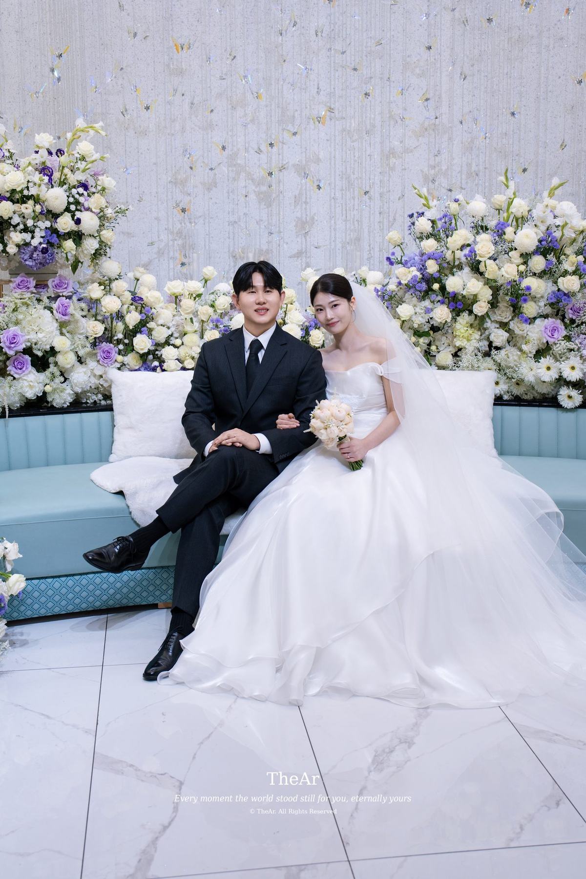 민트색 소파에 나란히 앉아 팔짱을 끼고 웃는 신랑과 신부