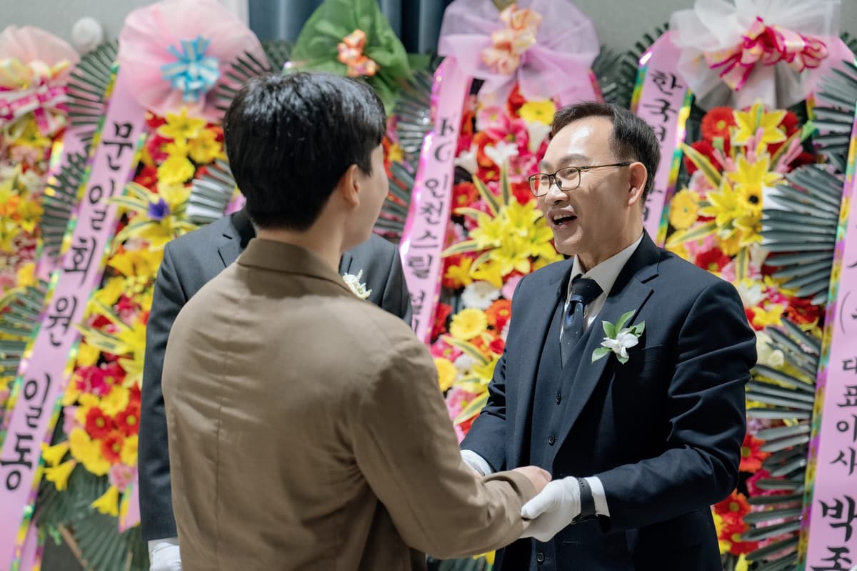 축하 화환이 늘어선 로비에서 하객과 두 손을 맞잡고 인사하는 신랑