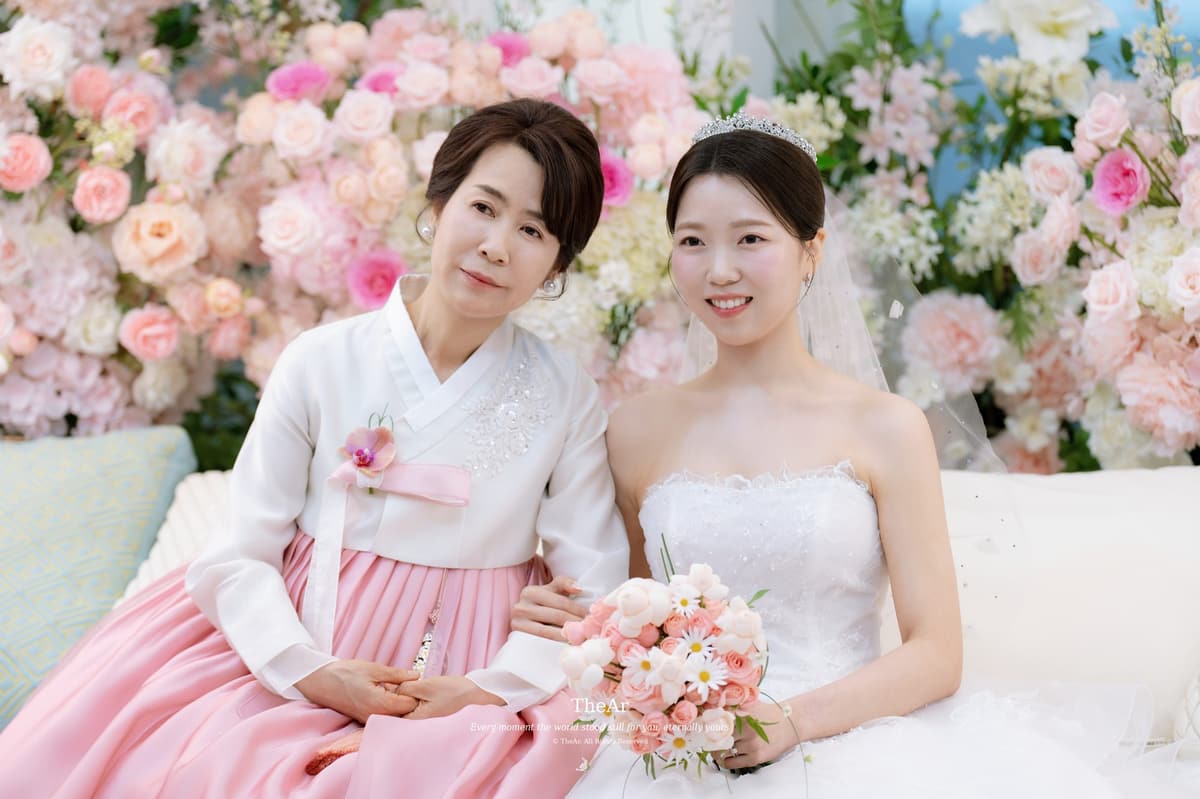 L65 가든홀 신부대기실 꽃 소파에서 한복 차림의 어머니와 손을 맞잡고 나란히 앉은 신부
