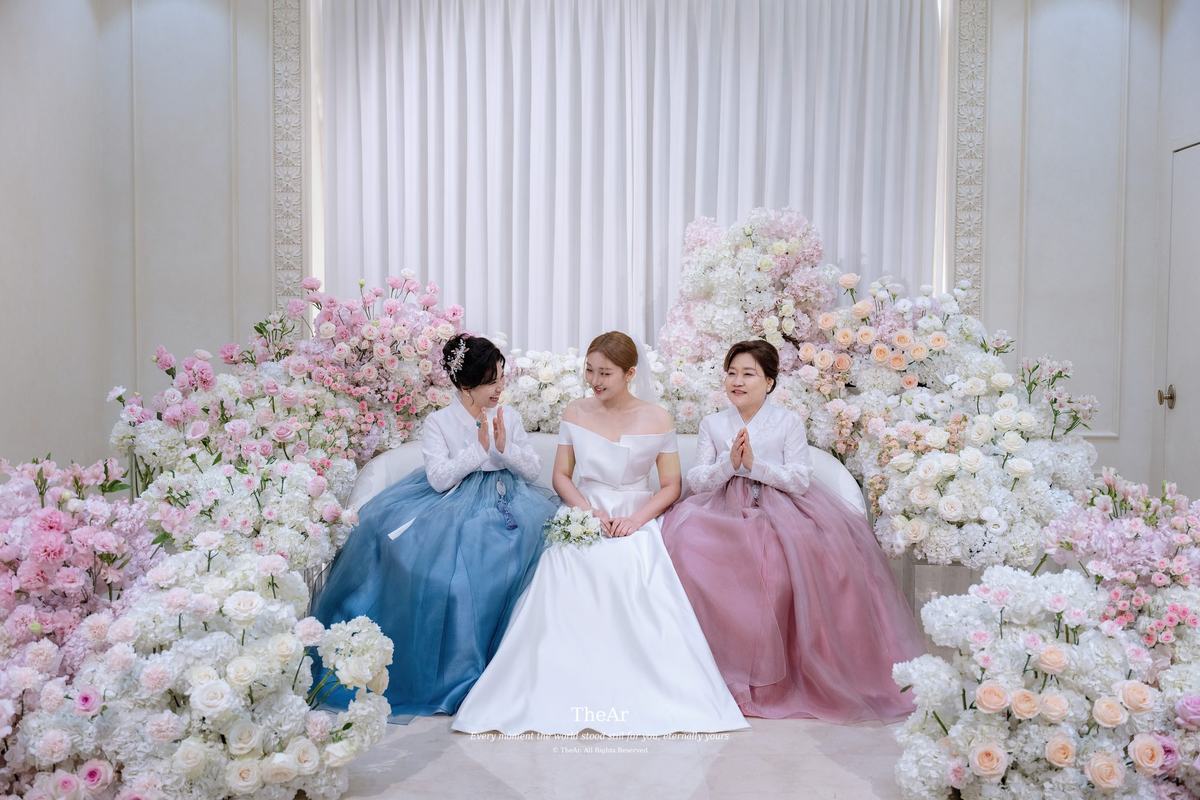 서울웨딩타워 신부대기실 꽃 소파에 한복 차림의 양가 어머니와 나란히 앉아 웃는 신부