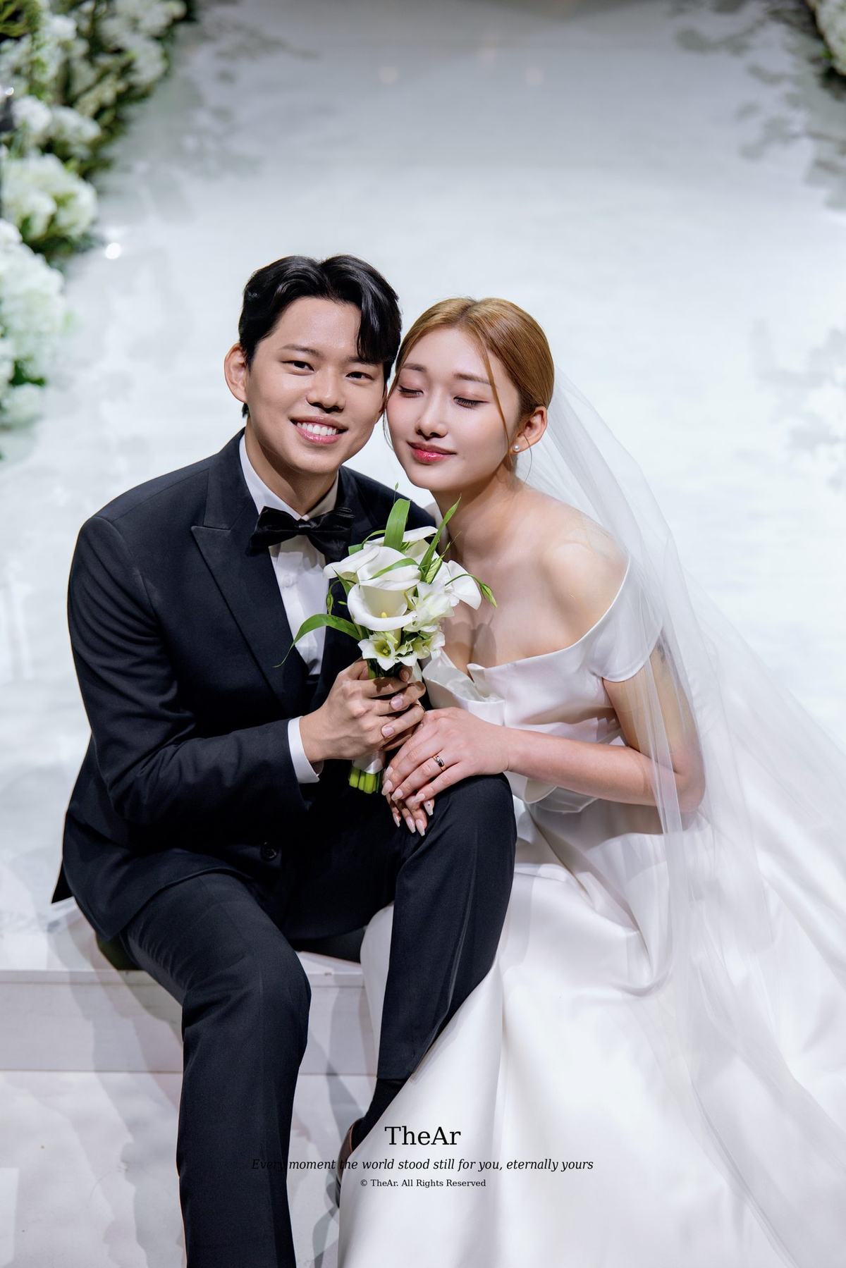 서울웨딩타워에서 부케를 함께 들고 나란히 앉아 서로에게 기대어 웃는 신랑과 신부