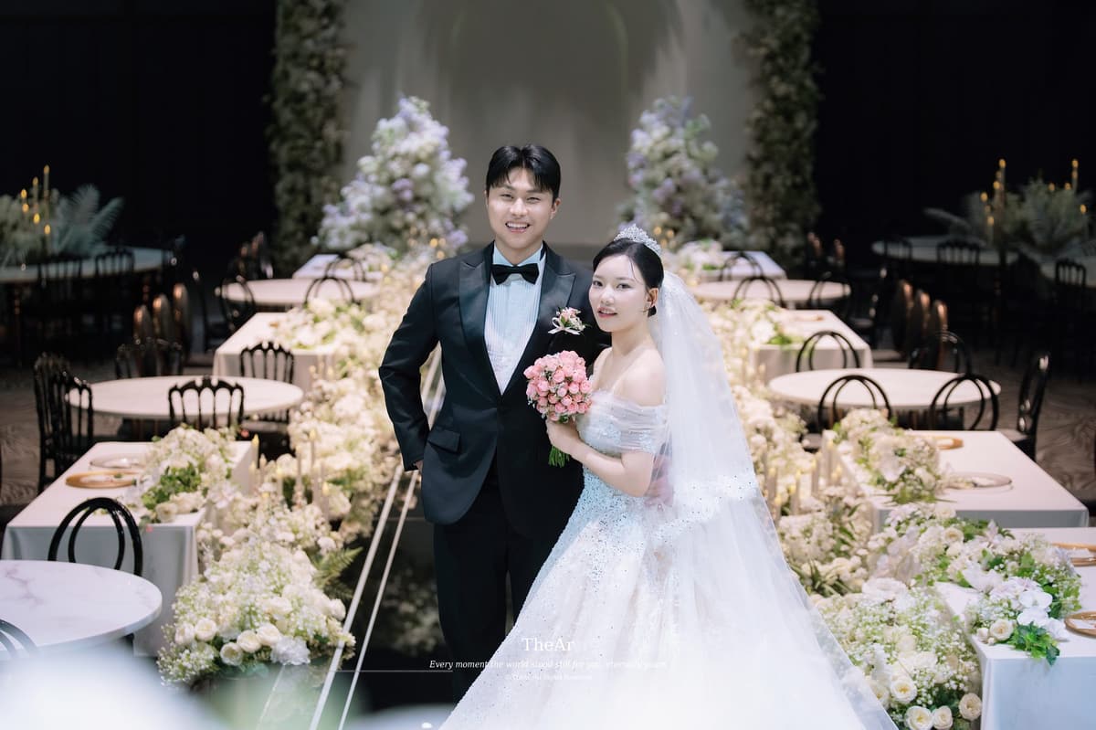 연회 테이블 사이로 놓인 버진로드에 나란히 서서 팔짱을 낀 신랑과 신부
