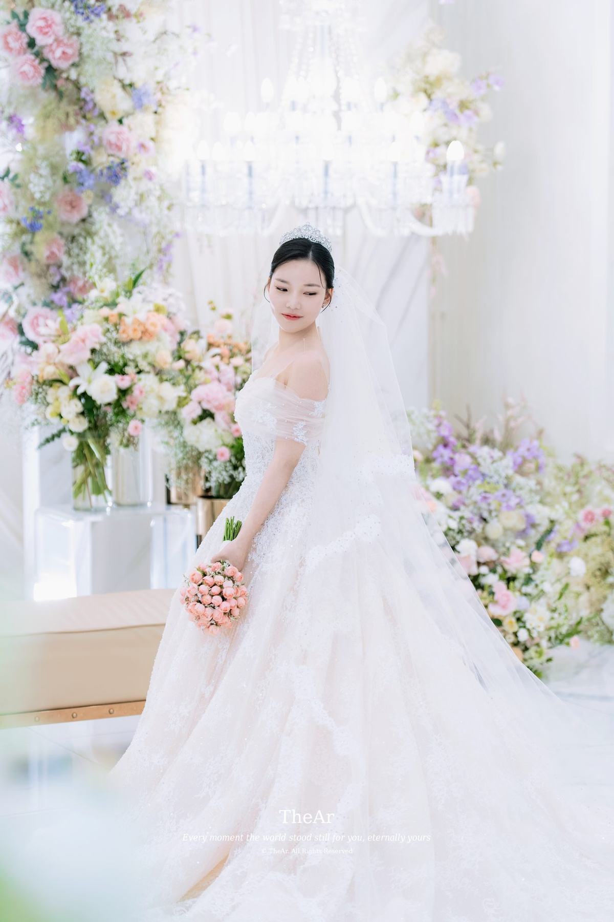 꽃 장식 사이에서 손에 든 부케를 내려다보는 신부의 옆모습