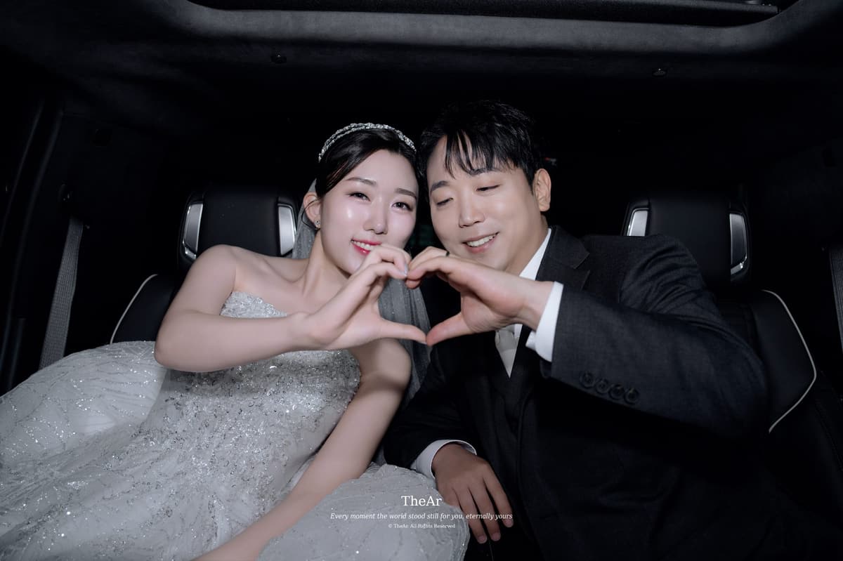이동하는 차 안에서 나란히 앉아 손으로 하트를 만드는 신랑과 신부